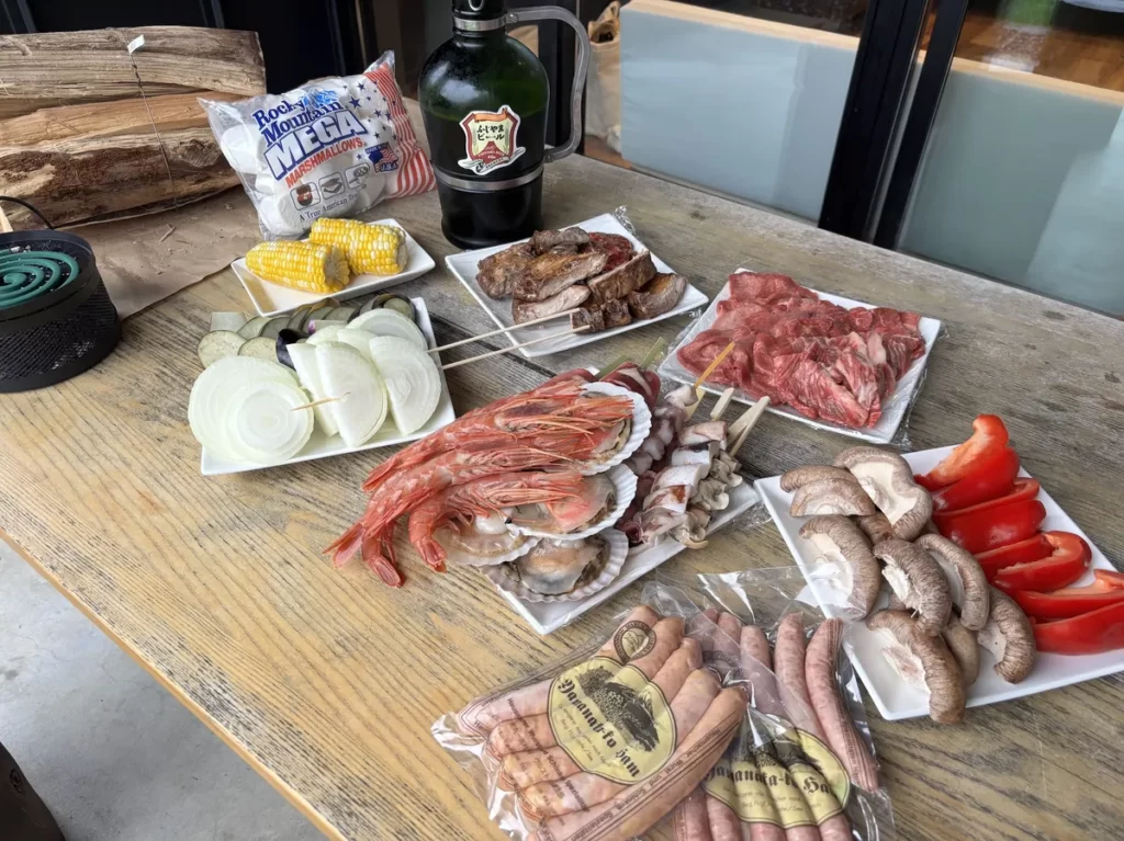 屋根付きBBQテラスの木製テーブルに用意された山中湖ハムのソーセージやエビ、ホタテ、野菜などの食材