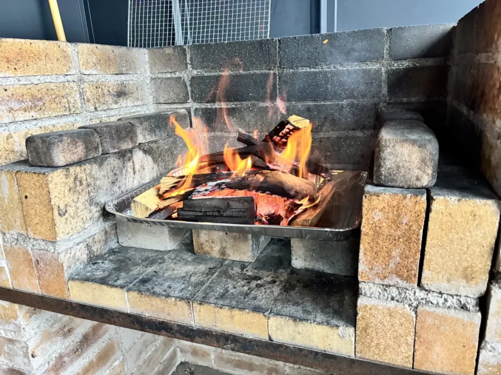 一棟貸し別荘のテラスに設置されたレンガ造りの本格的なBBQコンロで薪と炭が真っ赤に燃える様子